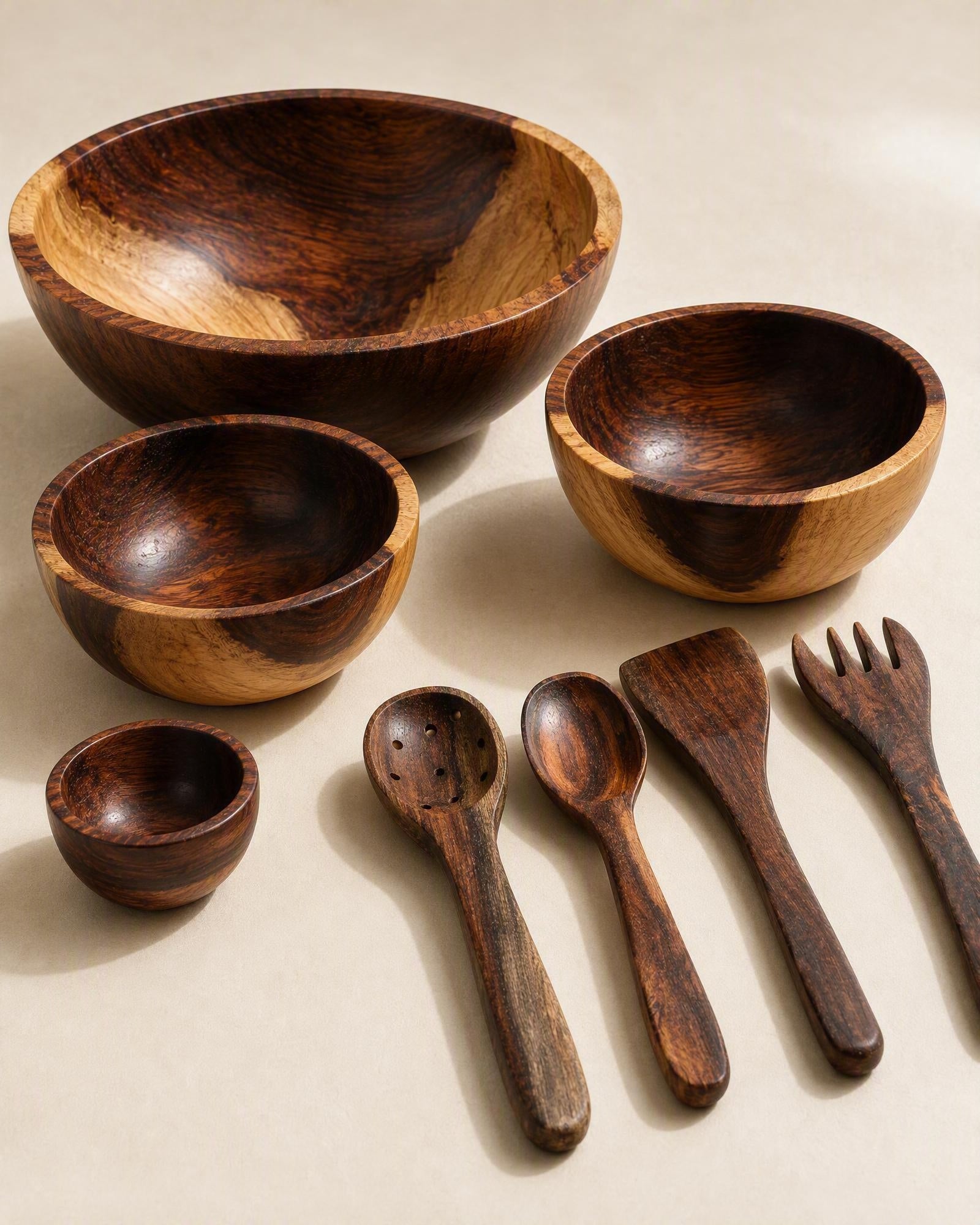 A set of handcrafted wooden dining utensils and bowls with rich dark brown and warm honey wood grain patterns, arranged on a neutral beige background.