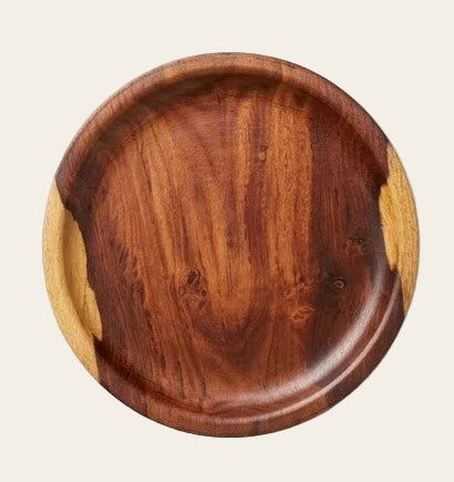 A round wooden serving platter with a rich dark brown center and contrasting light tan end grain, shown on a neutral light gray background.