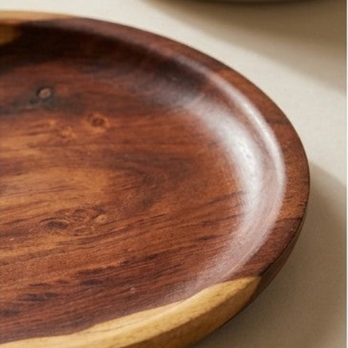 A close-up of a round wooden serving platter with a dark brown polished center and a natural light wood edge, resting on a neutral beige surface.