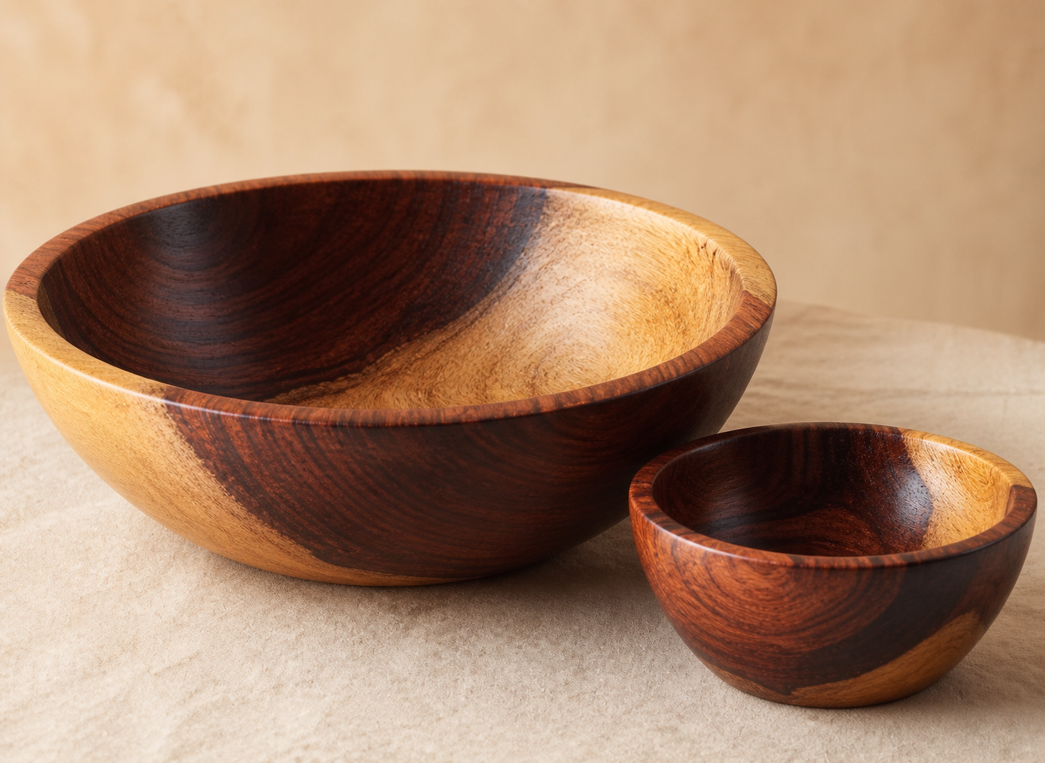 Two handcrafted wooden bowls with a rich dark brown and warm golden wood grain pattern, displayed on a neutral beige textured surface.