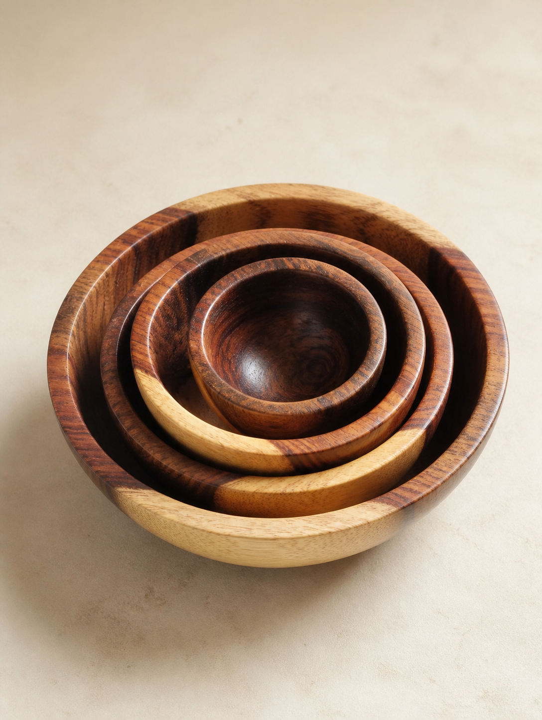 A set of five nested wooden bowls of varying sizes with natural wood grain patterns in shades of brown and beige, arranged on a light beige surface.