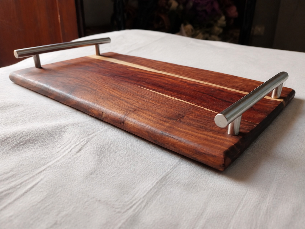 A rectangular wooden serving tray with a rich dark brown wood grain and two brushed silver metal handles, resting on a white fabric surface.