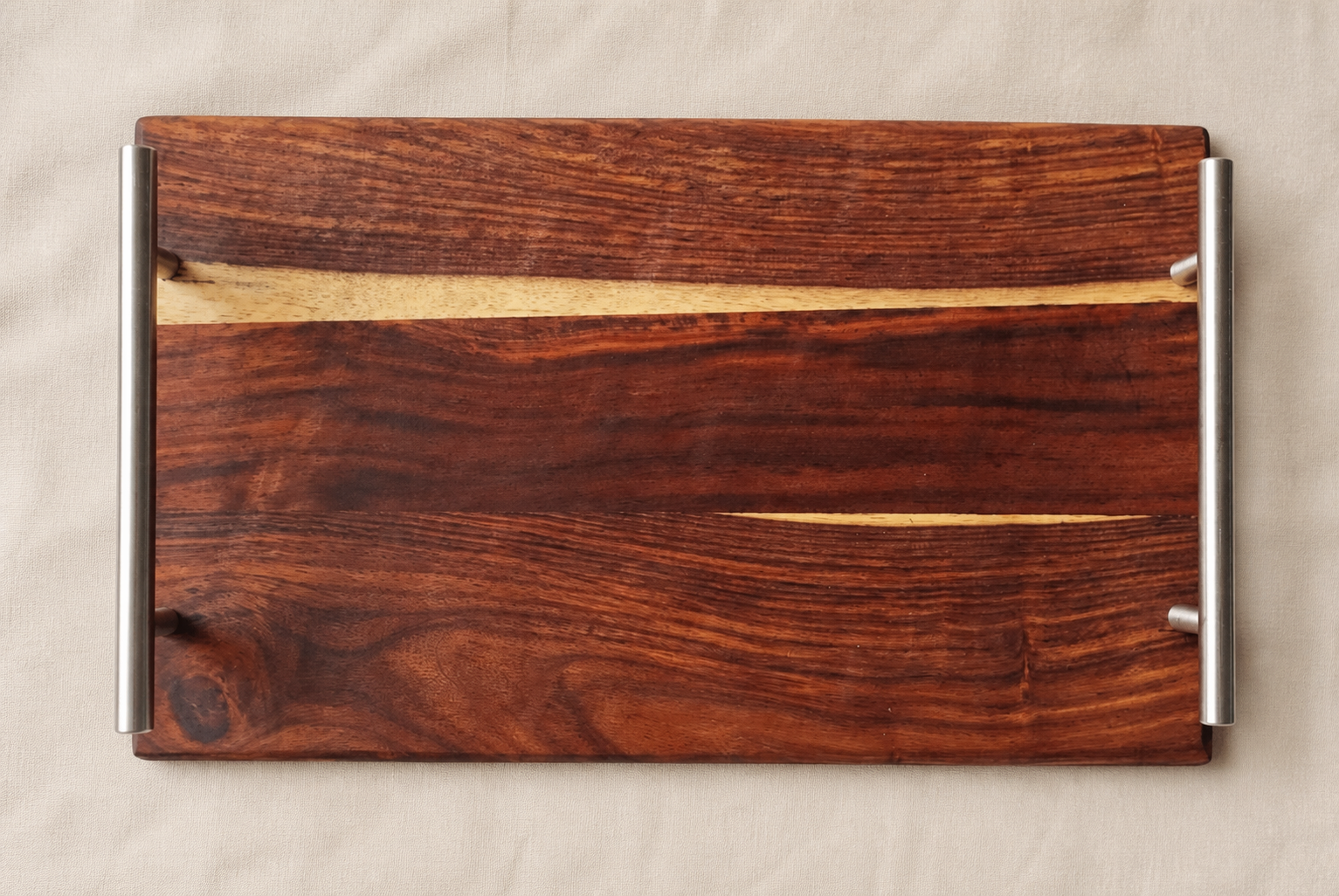 A rectangular wooden serving board or tray with a rich dark brown wood grain and two polished silver metal handles on the sides, displayed on a neutral beige fabric background.