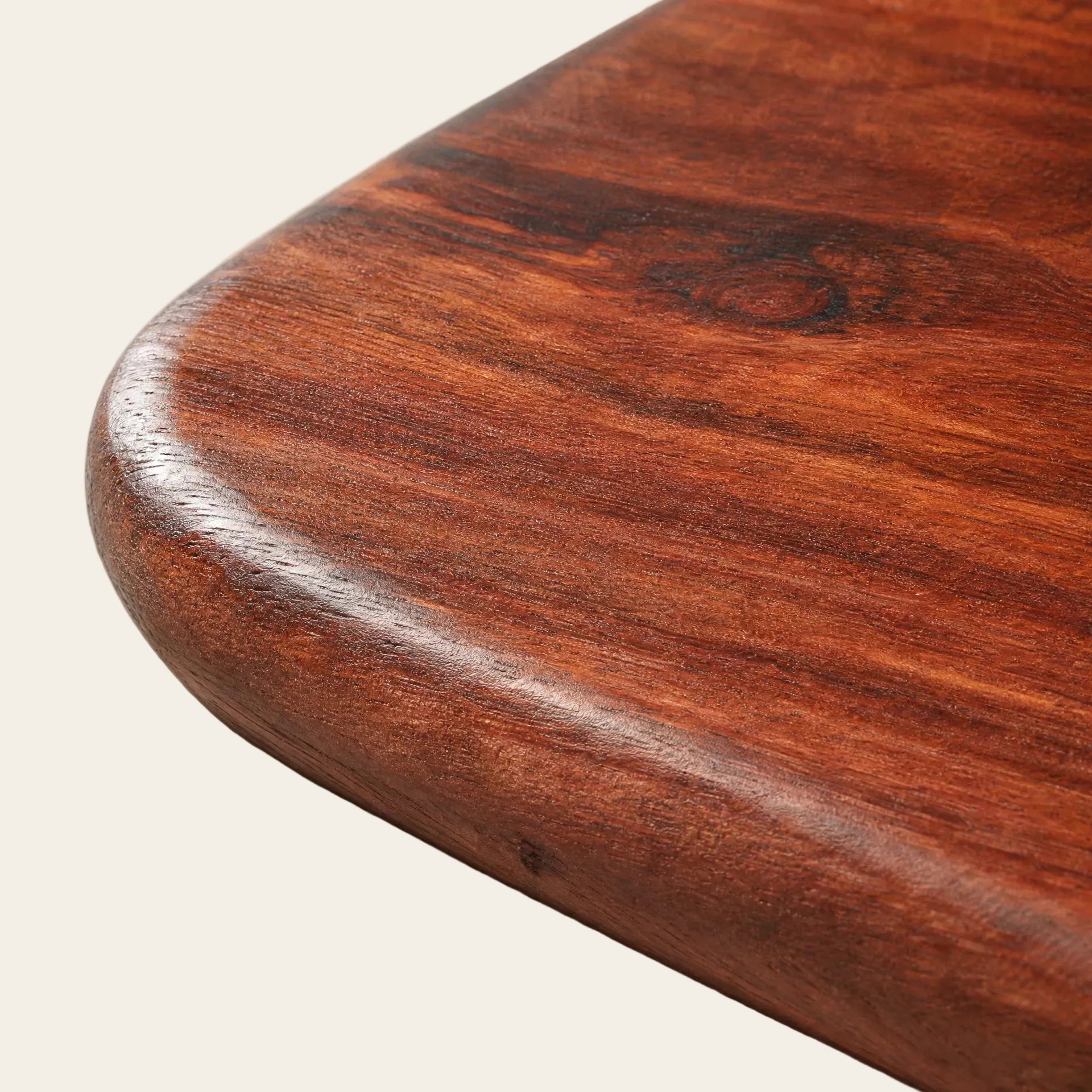 Close-up of a polished reddish-brown wooden board with rounded corners and visible wood grain, photographed on a light neutral background.
