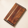 A rectangular wooden serving board with a rich dark brown grain pattern and two silver metal corner handles, shown on a light beige background.